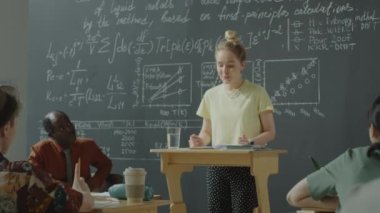 Kafkas kız kürsüde duruyor, notlar okuyor ve Afrikalı Amerikan profesörle matematik dersi sırasında bir grup öğrenciye konuşma yapıyor.