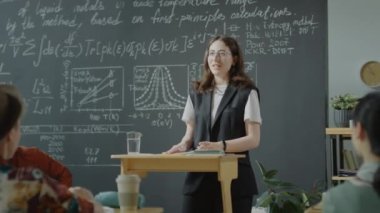 Afrika kökenli Amerikalı bir profesörle ders sırasında kürsüde durup grup arkadaşlarıyla konuşan beyaz bir kız öğrenci.