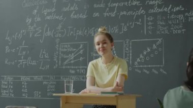 Kürsüde durup kameraya gülümseyerek poz veren neşeli üniversiteli kızın orta ölçekli fotoğrafı.