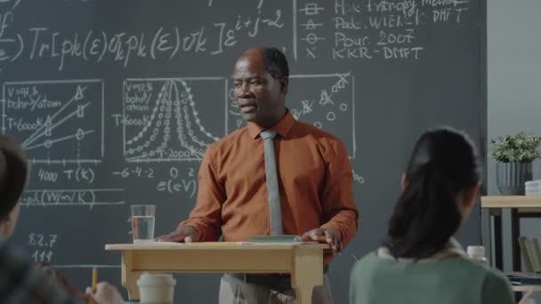 African American Professor Står Vid Föreläsaren Framför Tavlan Och Förklarar — Stockvideo