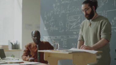 Genç öğrenci, üniversitede matematik dersinde sunum yaparken kürsüde durup notlar okuyor.