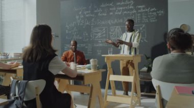 Afrika kökenli Amerikalı erkek öğrencinin kürsüde durduğu ve lisede çok ırklı profesör ve grup arkadaşlarına sunum yaptığı görüntüyü yakınlaştırın.