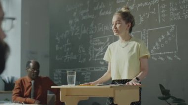 Kolej sınıfında kürsüde duran ve grup arkadaşları ve Afro-Amerikan profesörlerin önünde konuşan beyaz bir kız.