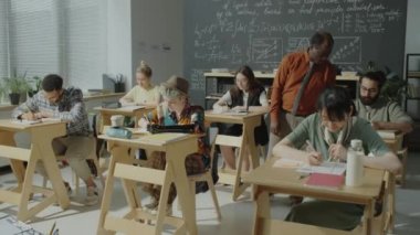 Afrika kökenli Amerikalı profesör sınıfta yürüyor ve çeşitli öğrencilere lisede sınav sırasında yardım ediyor.