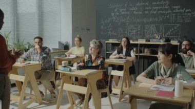Sınıfta sıralarda oturan ve ders sırasında Afrikalı Amerikalı profesörleri dinleyen çok ırklı üniversite öğrencileri grubu.