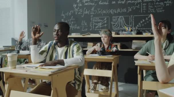 アフリカ系アメリカ人の学生が腕を上げて授業中に質問をする様子を撮影しながら 多民族グループの仲間と大学で勉強する — ストック動画
