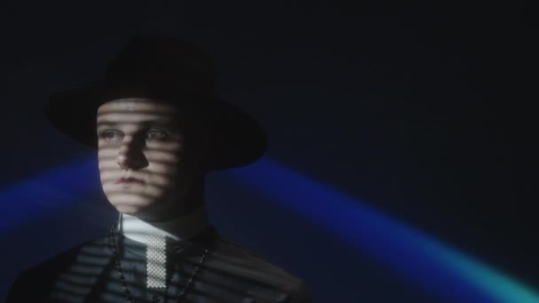 배경에 영사기를 어두운 스튜디오에 얼굴에 윈도우 블라인드 그림자와 모자를 남자의 — 비디오