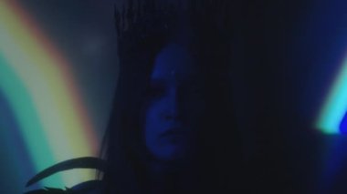 Gotik taç takan, tüylü, aydınlık projeksiyonlu, karanlık odada poz veren kadın.