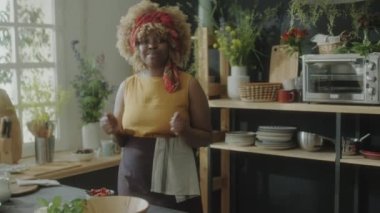 Önlüklü genç Afrikalı Amerikalı kadın mutfakta dikiliyor ve kameraya konuşuyor. Yemek vlog 'u çekerken ya da çevrimiçi aşçılık dersi verirken.