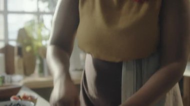 Önlüklü genç Afrikalı Amerikalı kadının ahşap kasede hamur yoğururken ve yemek tarifi çekerken kamera önünde konuşurken çekilmiş el kamerası görüntüleri.