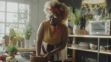 Önlüklü Afro-Amerikalı kadın hamuru ahşap kasede yoğuruyor ve kamera önünde konuşuyor mutfakta yemek tarifi çekerken.