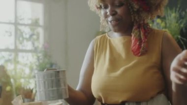 Neşeli Afrikalı Amerikalı kadın yemek blogcusu ahşap kasede un seçiyor, kamera önünde şarkı söylüyor ve mutfakta yemek tarifi çekerken dans ediyor.