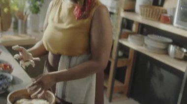 Önlüklü genç siyahi kadının ahşap kasede hamur yoğururken ve mutfakta mutfak vlog 'u çekerken kameraya yemek tarifi söylerken el kamerasını kaldır.
