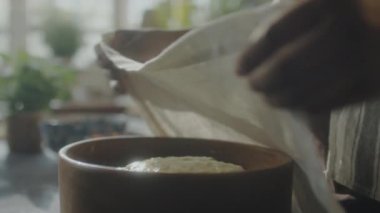 Afro-Amerikalı bir kadının, hamuru çay havlusuyla örterken ve mutfak masasından kase alırken yakın plan çekimleri.