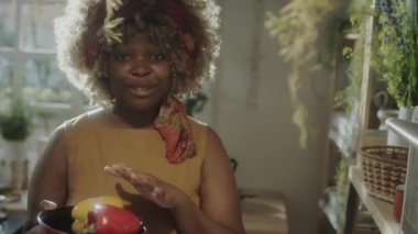 Afro-Amerikalı kadın yemek blogcusu fırına dolma biber koyuyor ve mutfakta çevrimiçi aşçılık mastırı yaparken kameraya konuşuyor.