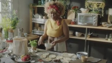 Afro-Amerikalı kadın yemek blogcusu silikon fırçayla hamuru yıkıyor ve çevrimiçi pişirme dersi verirken kameraya konuşuyor.
