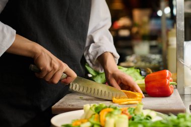 Genç bayan mutfak işçisinin elleri iş yerinde beklerken salata ya da başka bir yemek için taze sarı biber doğruyor.