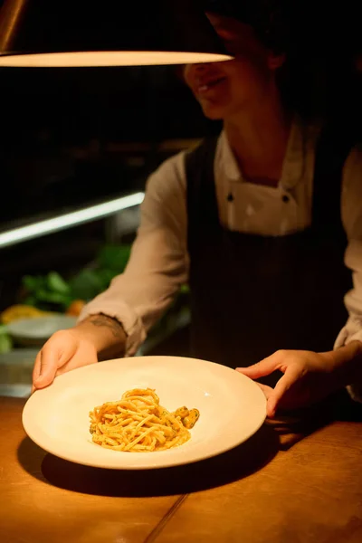 Focus on hands of young female worker of cafe passing plate with appetizing traditional Italian pasta cooked for guest of bistro