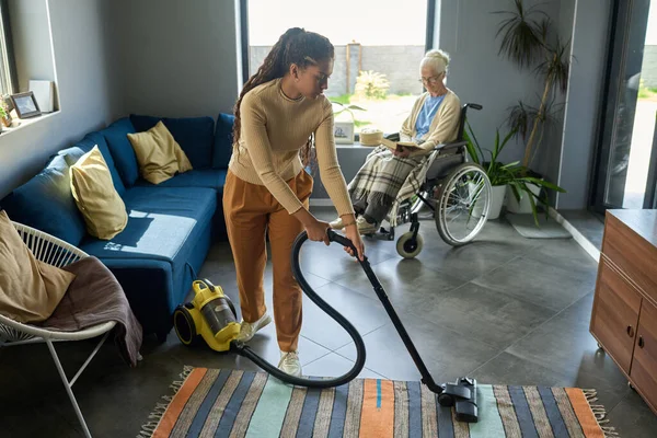 Gadis Muda Dengan Vacuum Cleaner Membantu Neneknya Dengan Kecacatan Dengan — Stok Foto