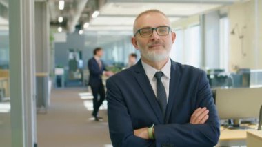 Formalite giymiş deneyimli kıdemli iş adamının belden yukarı pozu. Kolları çapraz duruyor ve iş günü kameraya poz veriyor.