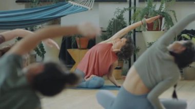 Genç kadınların grup kursunda kadın eğitmenle yoga yaptığı sahneler.