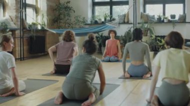 Yoga antrenmanı sırasında stüdyoda kadın öğretmenle birlikte kahraman pozu veren bir grup kadın.