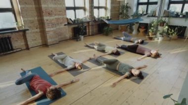 Spor kıyafetli bir grup kadının yoga stüdyosunda yalan söylerken yüksek açılı çekimleri.