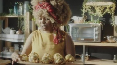Neşeli Afrika kökenli Amerikalı bir kadının yeni pişmiş çöreklerle çarşaf tutarken, iştah açıcı kokunun keyfini çıkarırken ve yemek blogu için video çekerken kamerada konuşurken.