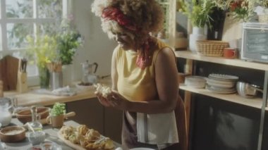 Orta boy Afrika kökenli Amerikalı bir kadının ev yapımı çörekleri yırtarken, kokunun tadını çıkarırken ve yemek tarifini çekerken kameranın karşısında konuşurken.