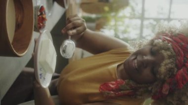 Afro-Amerikalı kadın yemek blogcusunun kamerada konuştuğu, ahşap kasede un elediği ve mutfakta yemek tarifi çekerken dans ettiği dikey çekim.