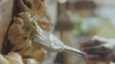 Afro-Amerikalı kadın yemek blogcusu sarımsaklı çörekleri sarımsaklı tereyağlı fırçalarken, gülümserken ve konuşurken çevrimiçi aşçılık ana sınıfı sunarken dikey çekim.