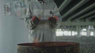 Sakallı evsiz adamın ateş fıçısının üstünde ellerini ısıtırken ve terk edilmiş binada kameraya poz verirken çekilen görüntüler.