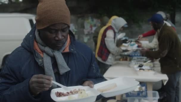 アフリカ系アメリカ人ホームレスの男性が市内のボランティアが提供する無料食事を食べる — ストック動画