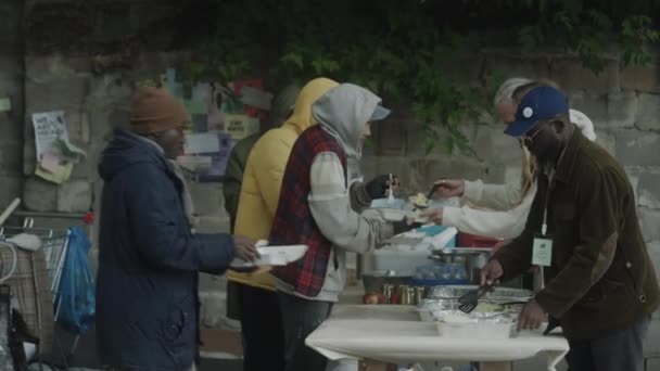 路上のスープキッチンでホームレスのための無料食事を提供するボランティアの広いショット — ストック動画