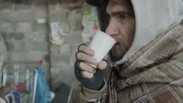 路上で立っている間に プラスチック製のカップから飲む髭のホームレスの男の胸を撃ち上げ 罰則を見て — ストック動画