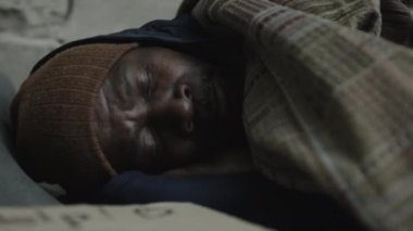 Örgü şapkalı, paçavralar içinde yerde uyuyan Afro-Amerikalı evsiz adamın yakın çekimi.