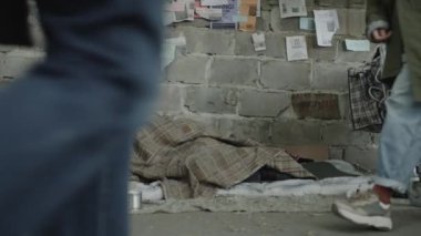 Evsiz bir dilenci sokakta yürürken ve onun için metal kutuya para bağışlarken yerde paçavralar içinde uyuyor.