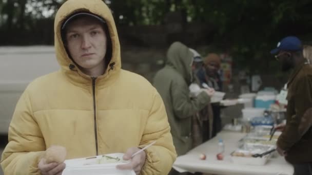 若いですホームレスの男の肖像 無料の食べ物を容器に保持し スープキッチンの近くにカメラのためにポーズ — ストック動画