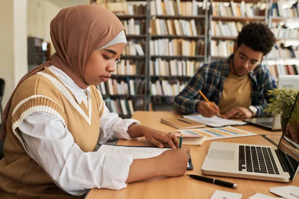 イスラム教徒の女の子でヒジャーブ書き試験でテーブルで他の学生とともにクラス — ストック写真
