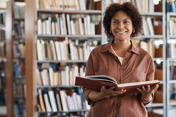 図書館で本を読みながらカメラで微笑むアフリカ系アメリカ人学生の肖像 — ストック写真