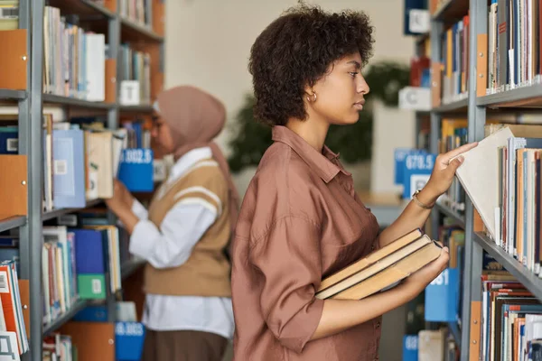 棚の近くに立って図書館で勉強する本を探しているアフリカ系アメリカ人の学生 — ストック写真