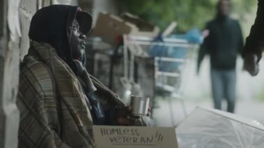 Afro-Amerikan bir adam sokakta evsiz dilenciye bağışta bulunuyor ve onu güzel sözlerle destekliyor.
