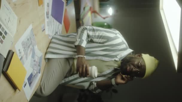 Pionowe Ujęcie Afroamerykańskiego Projektanta Siedzącego Biurku Trzymającego Filiżankę Kawy Rozmawiającego — Wideo stockowe