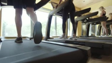 Spor salonunda antrenman yaparken koşu yapan ve yürüyen bir grup kadın ve erkeğin düşük açılı çekimi.
