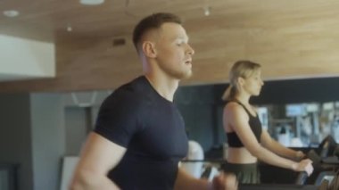 Spor kıyafetli kaslı bir adamın spor salonunda spor yaparken koşu bandında koşarken belini kaldırması.