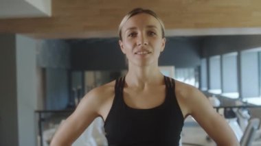 Spor kıyafetli neşeli bir kadının portresi spor salonunda gülümseyerek kameraya poz veriyor.