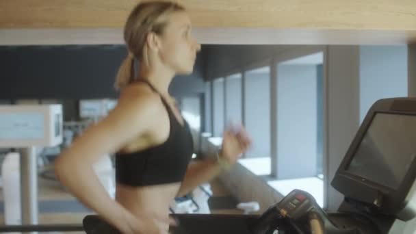 サイドビューウエストアップスポーツウェアの歩くとジムワークアウトを持っている間にトレッドミル上で実行中の運動女性のショット — ストック動画