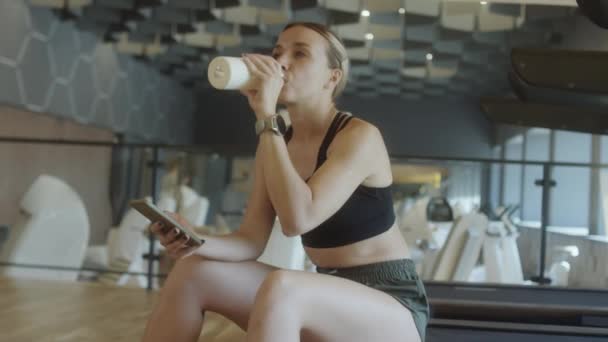 Vrouw Sportkleding Zittend Loopband Sportschool Drinkwater Uit Fles Typen Mobiele — Stockvideo