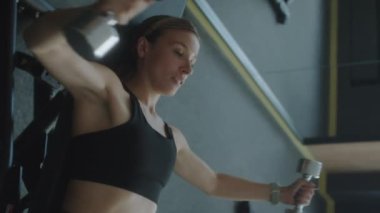 Spor kıyafetli bir kadının spor salonunun eğimli tezgahında dambıl sineği egzersizi yaptığı dikey çekim.