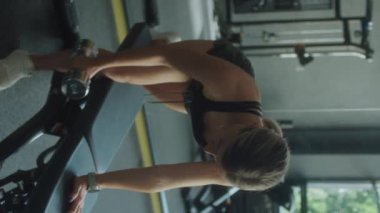 Spor kıyafetli bir kadının spor salonunda tek kollu halterli sıra egzersizi yaparken dikey çekimi.